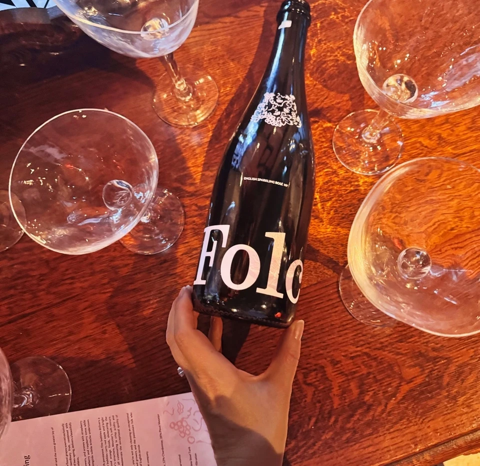 Folc English sparkling rosé bottle held above a wooden tasting table with glasses and tasting notes