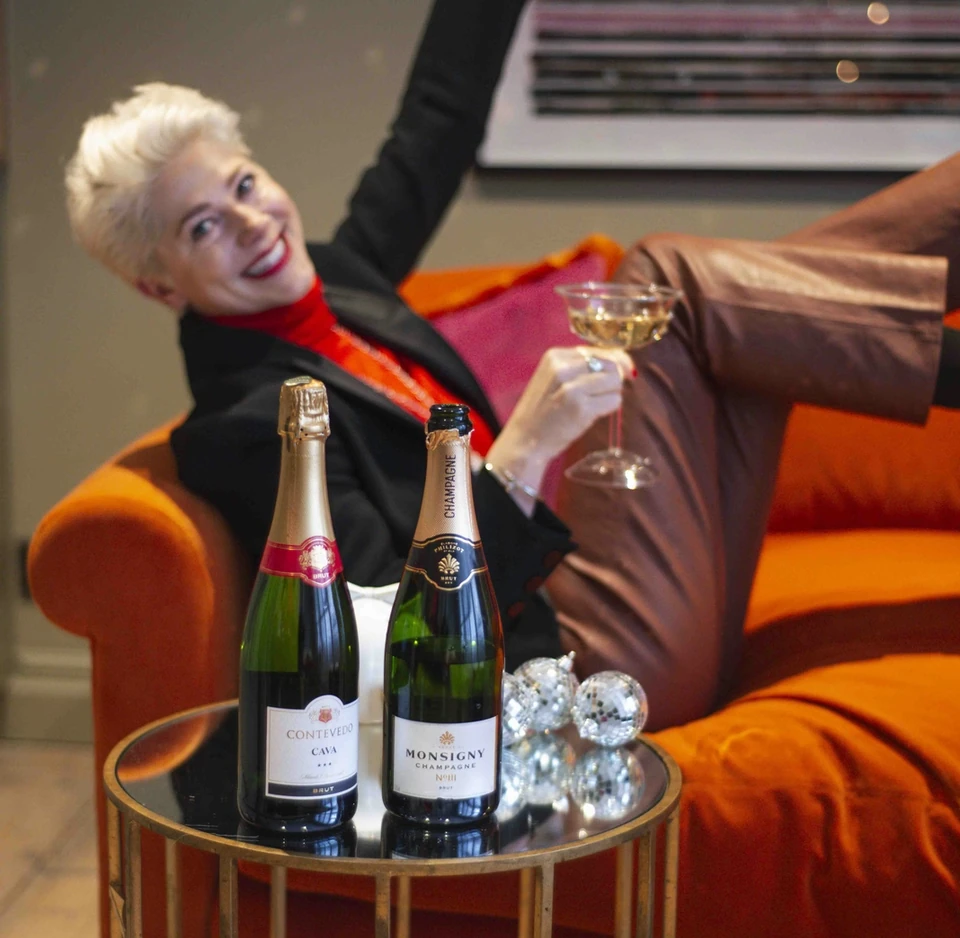 Person raising a disco ball beside two sparkling wine bottles in a bright orange seating area