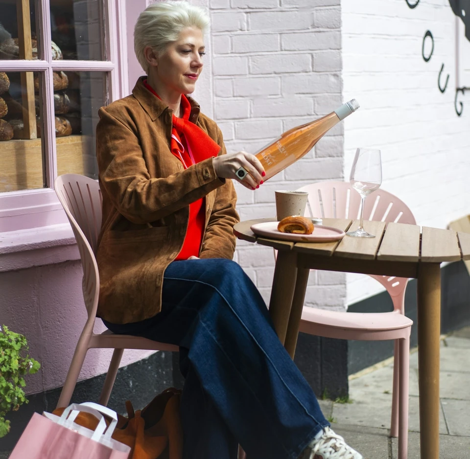 Person seated at a café table holding a bottle of Bolney Rosé beside a wine glass and pastry