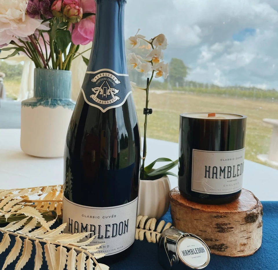 Hambledon sparkling wine bottle and candle beside flowers by a window