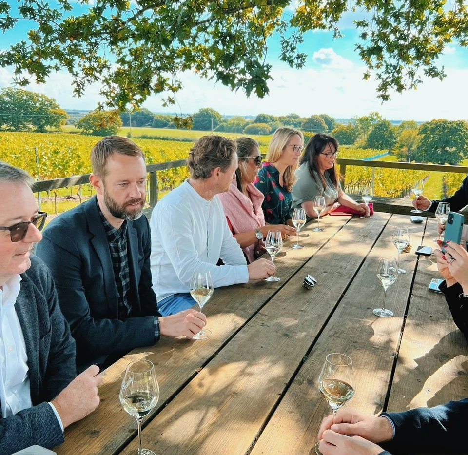 Group tasting wine at a vineyard table overlooking rows of vines