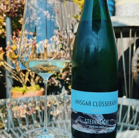 An Ansgar Clüsserath Steinreich Riesling bottle beside a glass of white wine outdoors