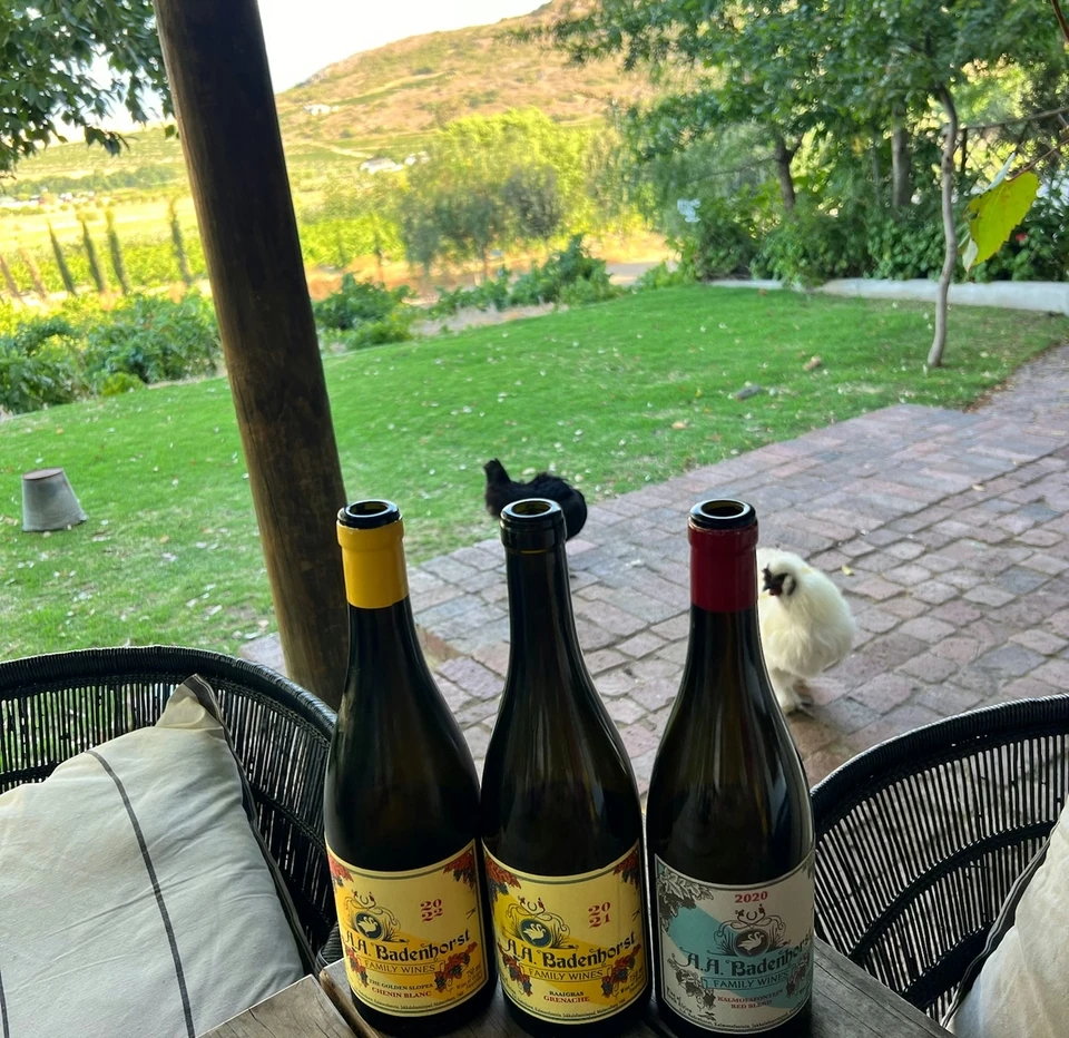 Three A.A. Badenhorst wine bottles on a table overlooking a vineyard