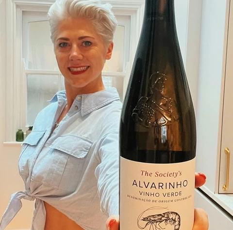 Woman holding a bottle of The Society's Alvarinho Vinho Verde in a bright kitchen