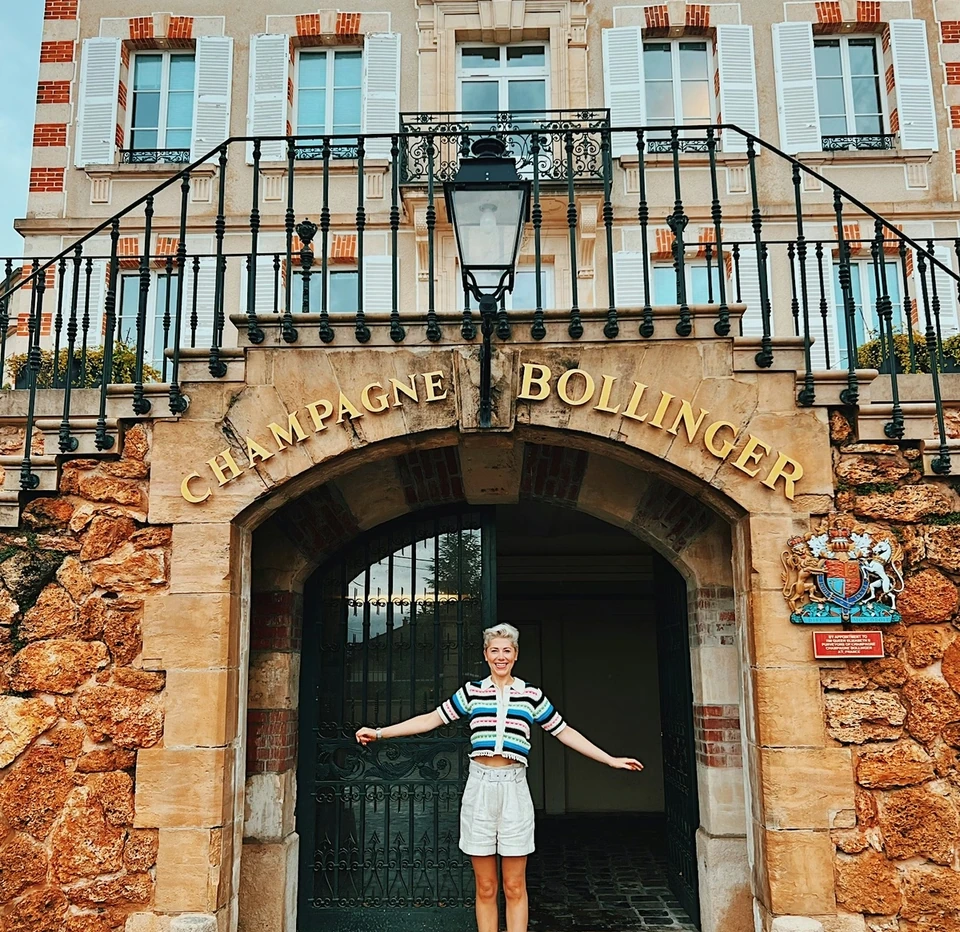 Person standing beneath the Champagne Bollinger entrance in a striped top and white shorts