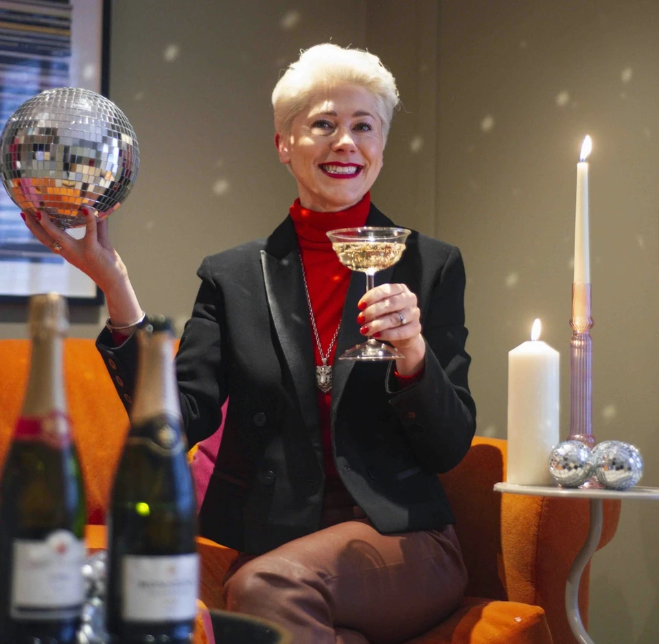 Woman holding a disco ball and sparkling wine beside lit candles