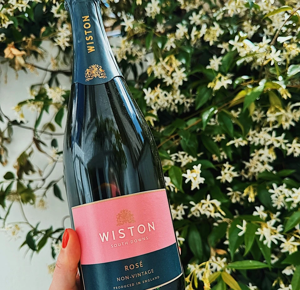 Wiston Rosé sparkling wine bottle held in front of flowering jasmine