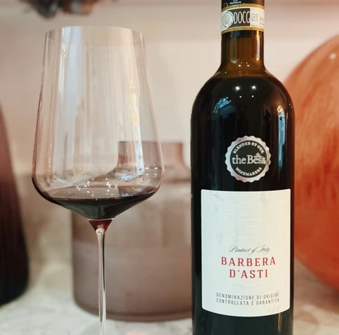 Bottle of Barbera d’Asti beside a glass of red wine on a marble table