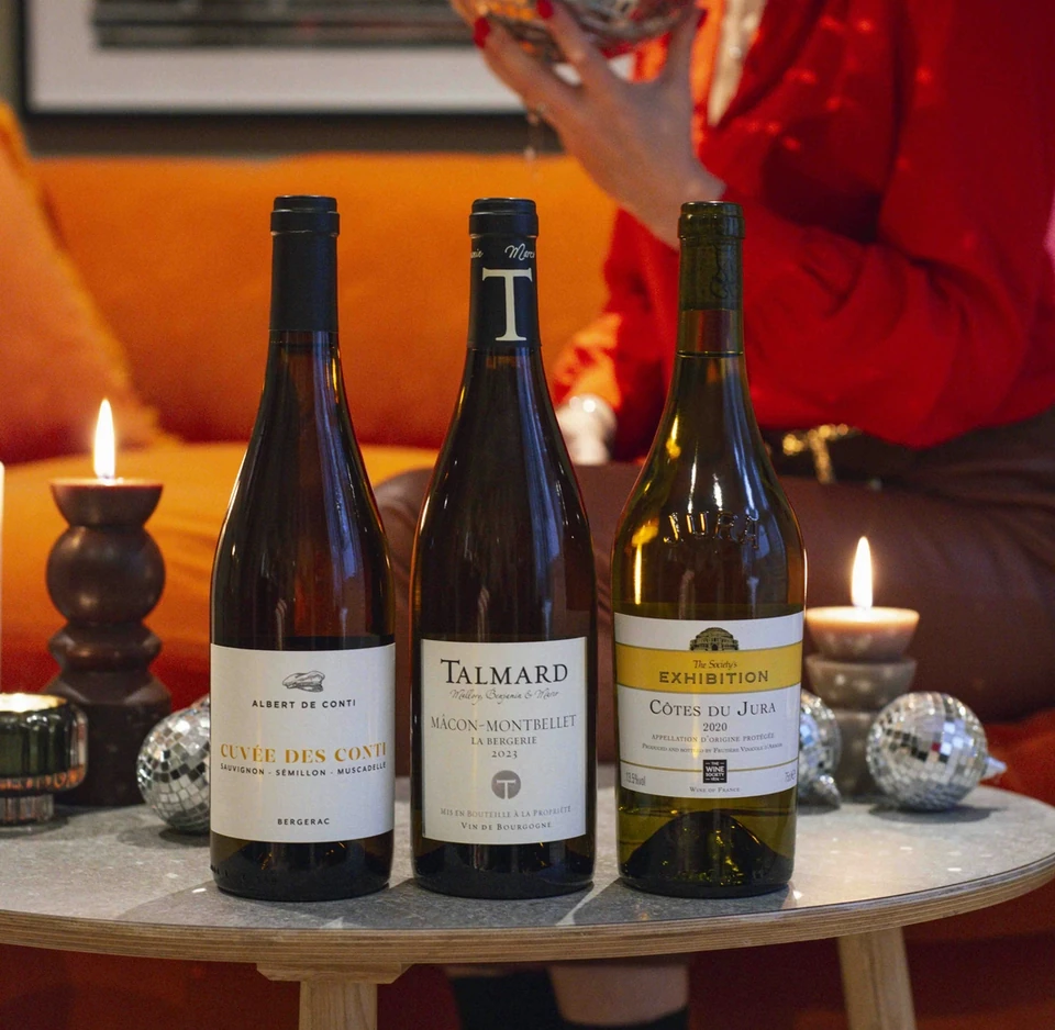 Three wine bottles on a table with candles, disco balls and a person in red holding a mirrored sphere