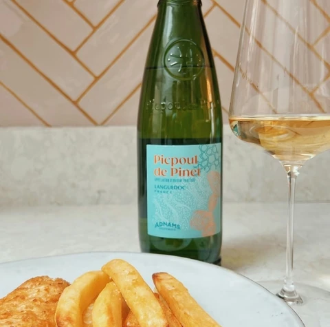 A bottle of Picpoul de Pinet beside a glass of white wine and fish and chips
