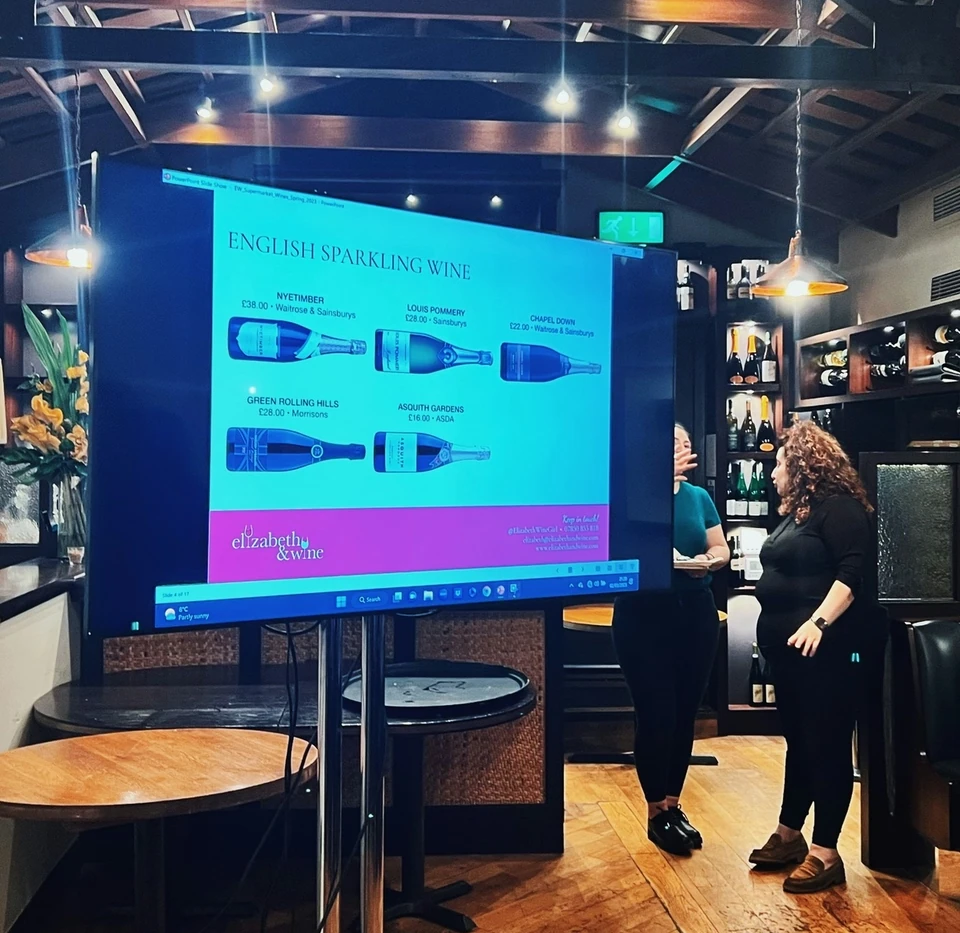 English sparkling wine tasting presentation on a screen in a bar, with two people beside it