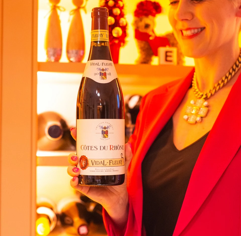 Woman holding a Vidal-Fleury Côtes du Rhône bottle in front of a wine display