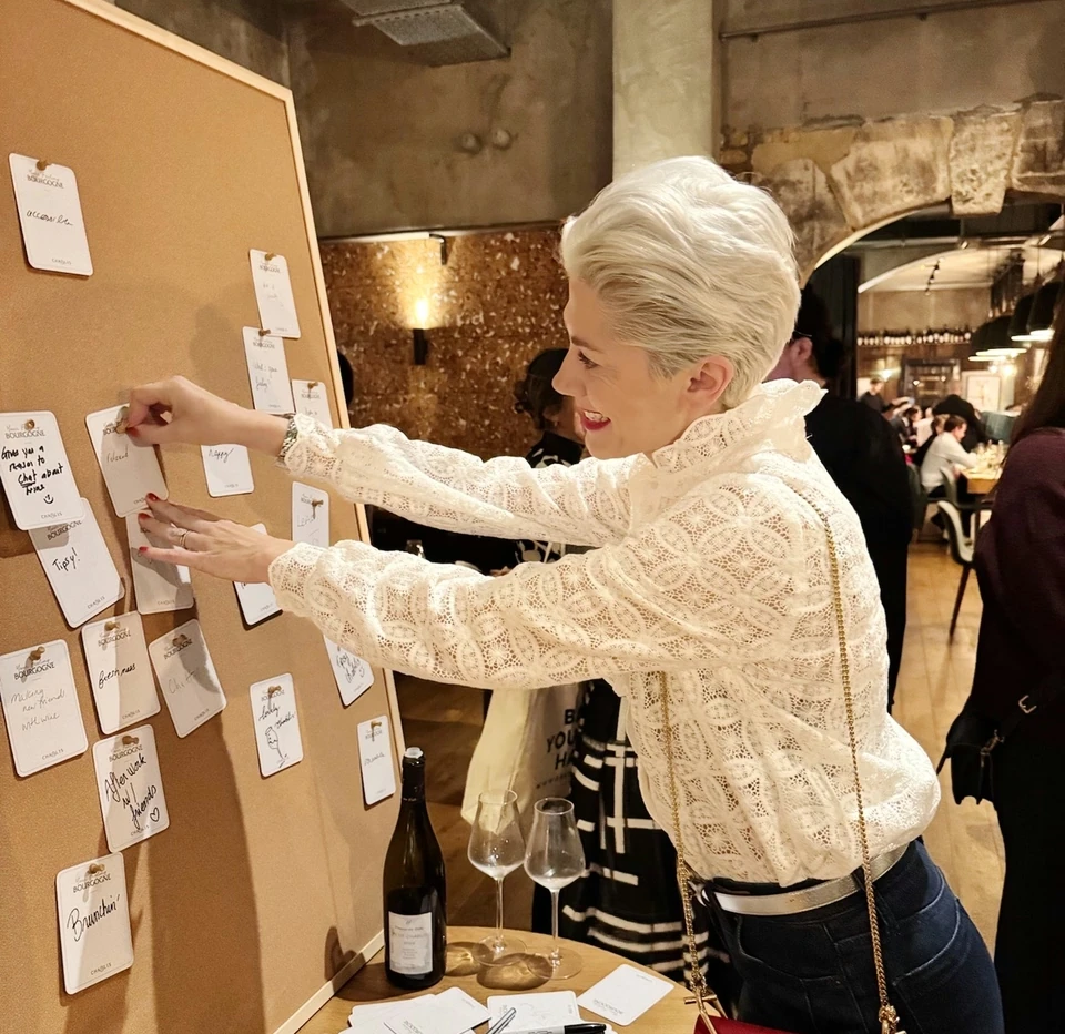 Woman arranging handwritten tasting cards beside wine glasses and a bottle at a Chablis tasting