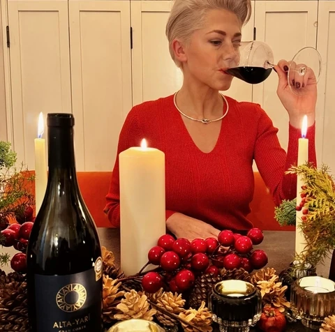Woman in a red jumper tasting red wine beside candles and an Alta-Yari bottle