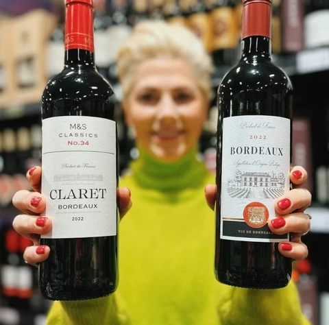 Two bottles labelled Claret and Bordeaux held up in a wine shop