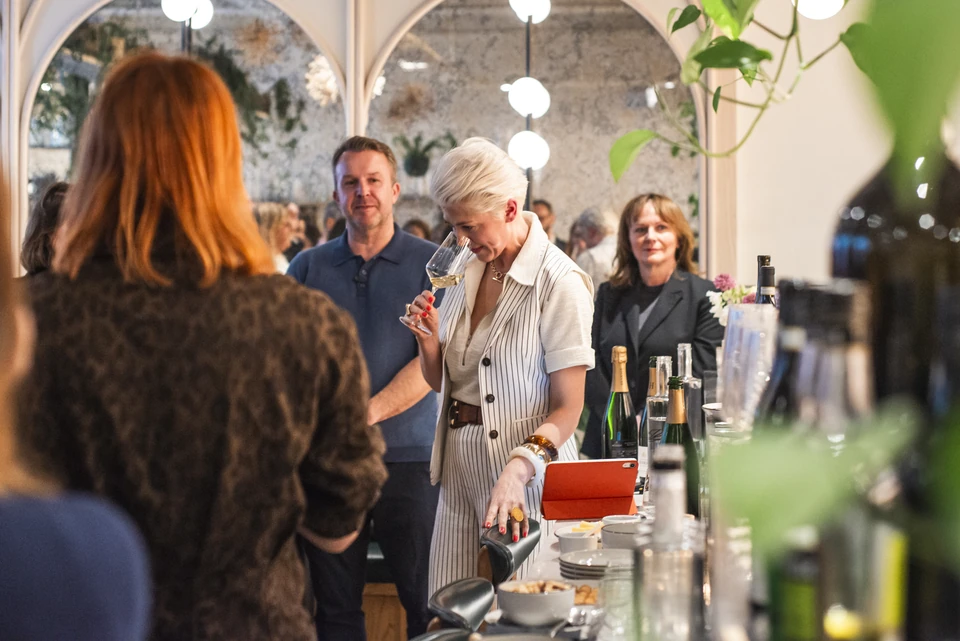 Guests gather around the bar at a wine tasting at Stem + Stem, with one guest smelling a glass of wine