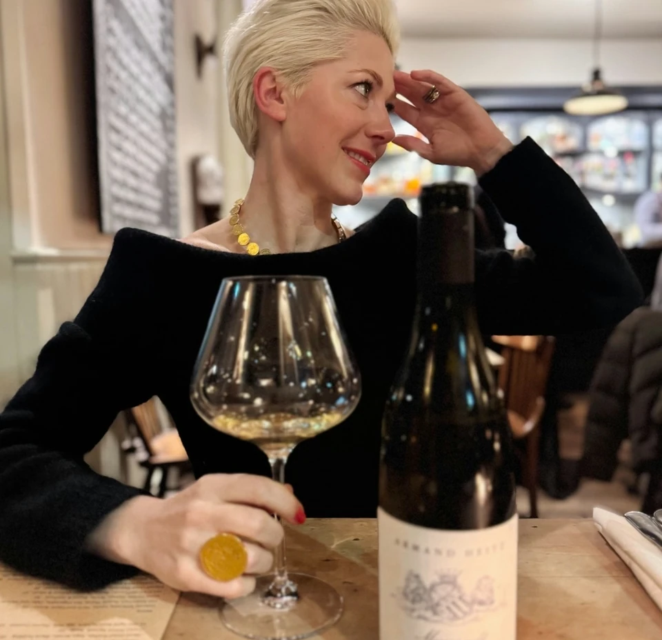 Woman in black holding a glass of white wine beside a bottle at a restaurant table