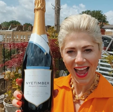 Woman in an orange shirt holds a bottle of Nyetimber Classic Cuvée outdoors