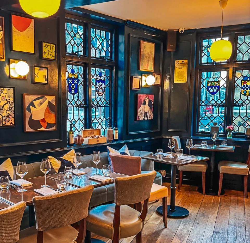 Elegant interior of Clarette restaurant in London with stained-glass windows, wine glasses and neatly laid tables