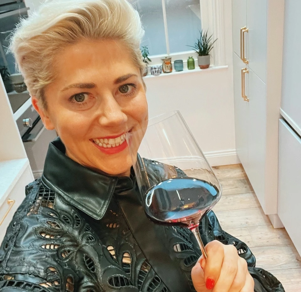 Woman holding a glass of red wine in a bright kitchen
