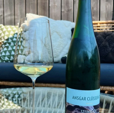 Ansgar Clüsserath Steinreich Riesling bottle beside a glass of white wine on an outdoor table