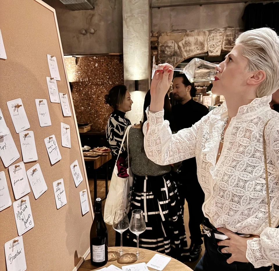 Guest tasting white wine beside a board of handwritten Burgundy notes