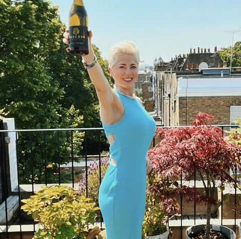 Woman in a blue dress holds a Sorcova wine bottle on a sunny terrace