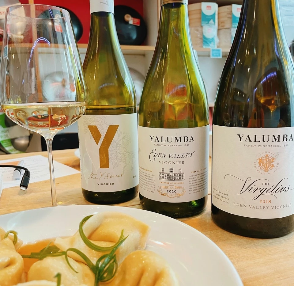 Three Yalumba Viognier bottles and a glass of wine beside dumplings