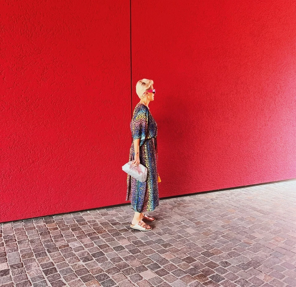 Person in a patterned dress walking beside a vivid red wall