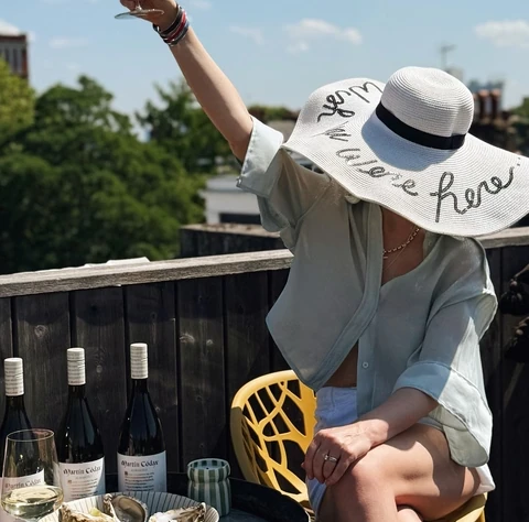 Person raising a glass of white wine beside Martin Códax bottles and oysters outdoors