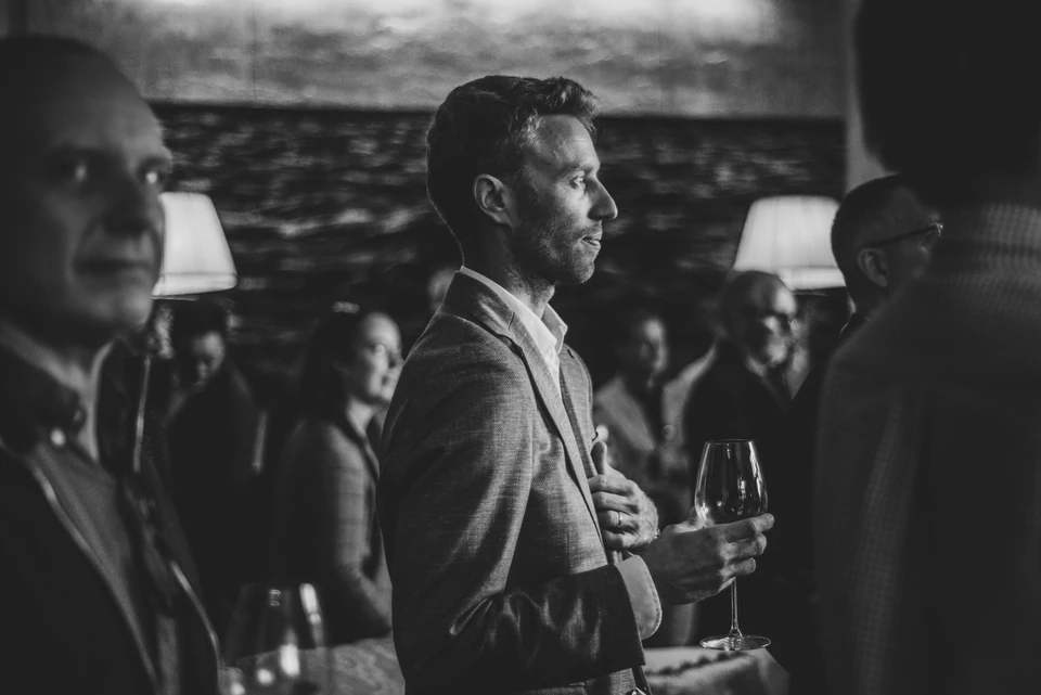 Guests mingle indoors at a wine launch event, with a man holding a glass of wine