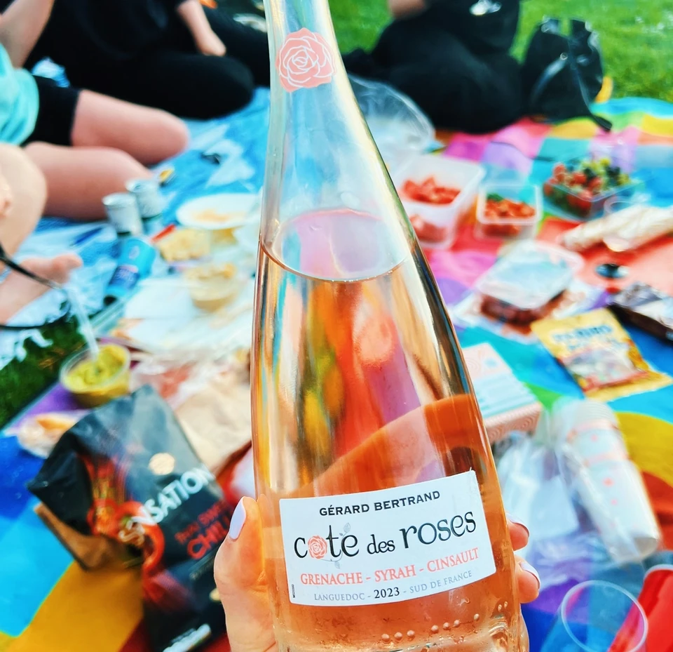 Bottle of Gérard Bertrand Côte des Roses Grenache rosé held above a colourful picnic