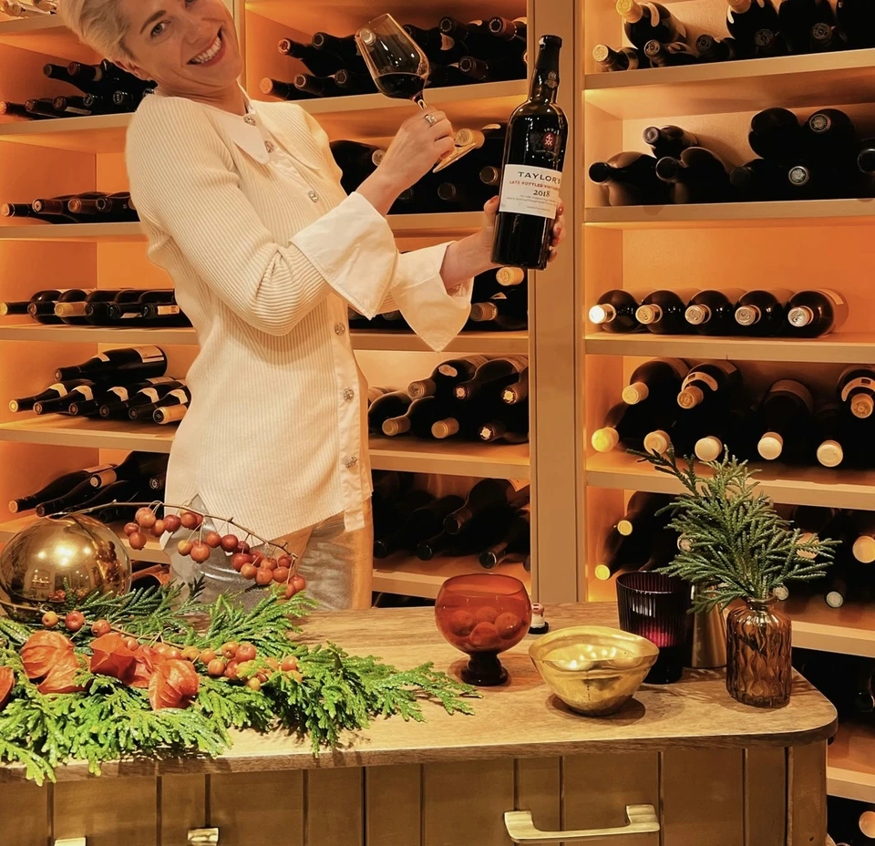 Woman holding a bottle of Taylor's Late Bottled Vintage 2018 Port beside a glass in a festive wine room