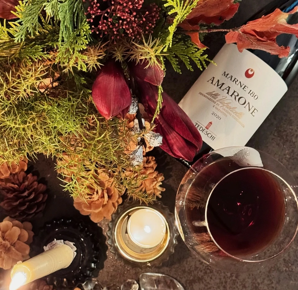 Tedeschi Amarone della Valpolicella bottle and red wine glass with foliage, dried flowers and candles