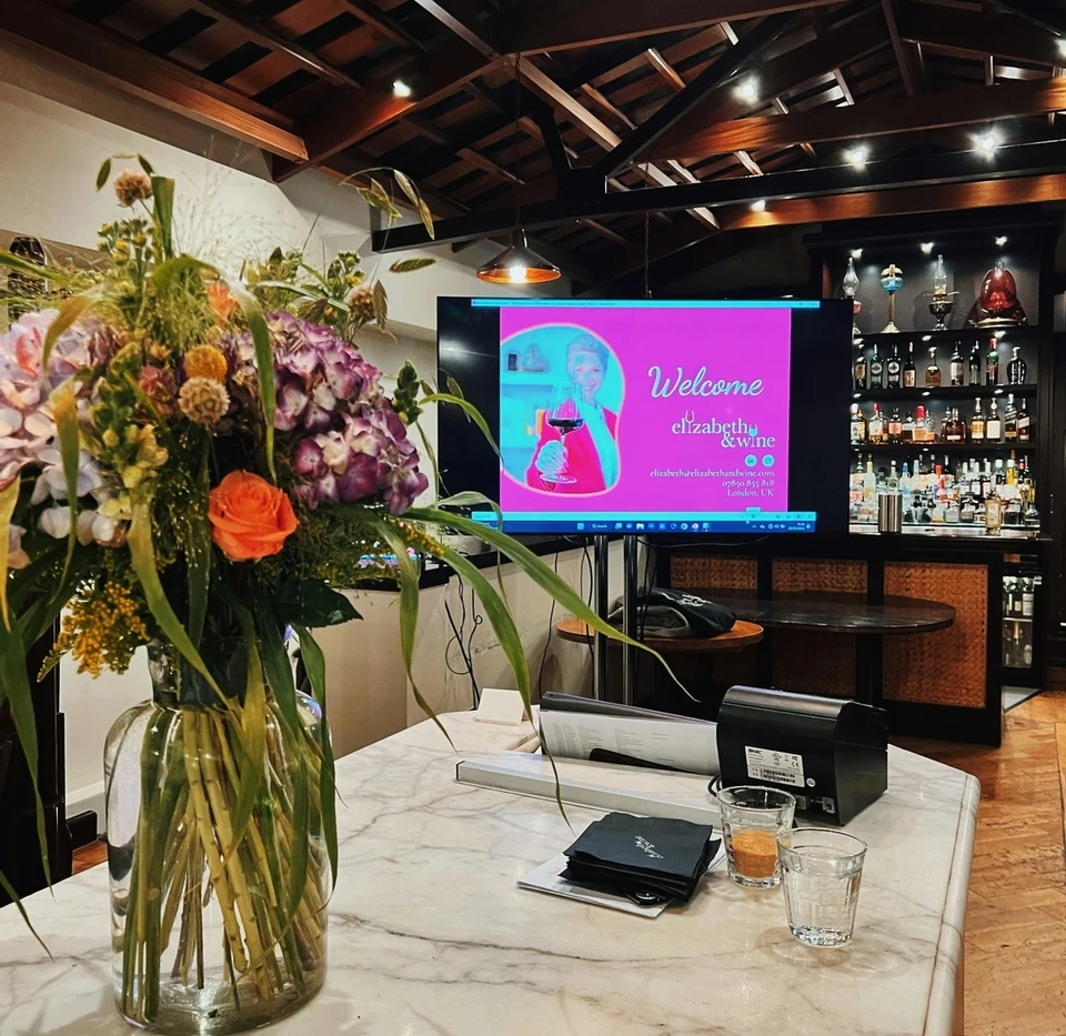 Marble bar with flowers and a screen displaying a welcome slide for an Elizabeth & Wine tasting
