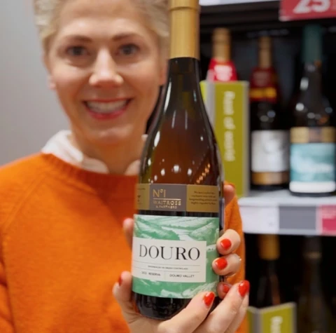 Woman in an orange jumper holding a bottle of Waitrose No.1 Douro wine in a shop