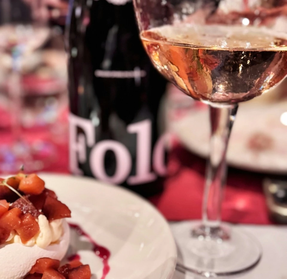 Glass of sparkling rosé beside a dessert plate and a Folc wine bottle