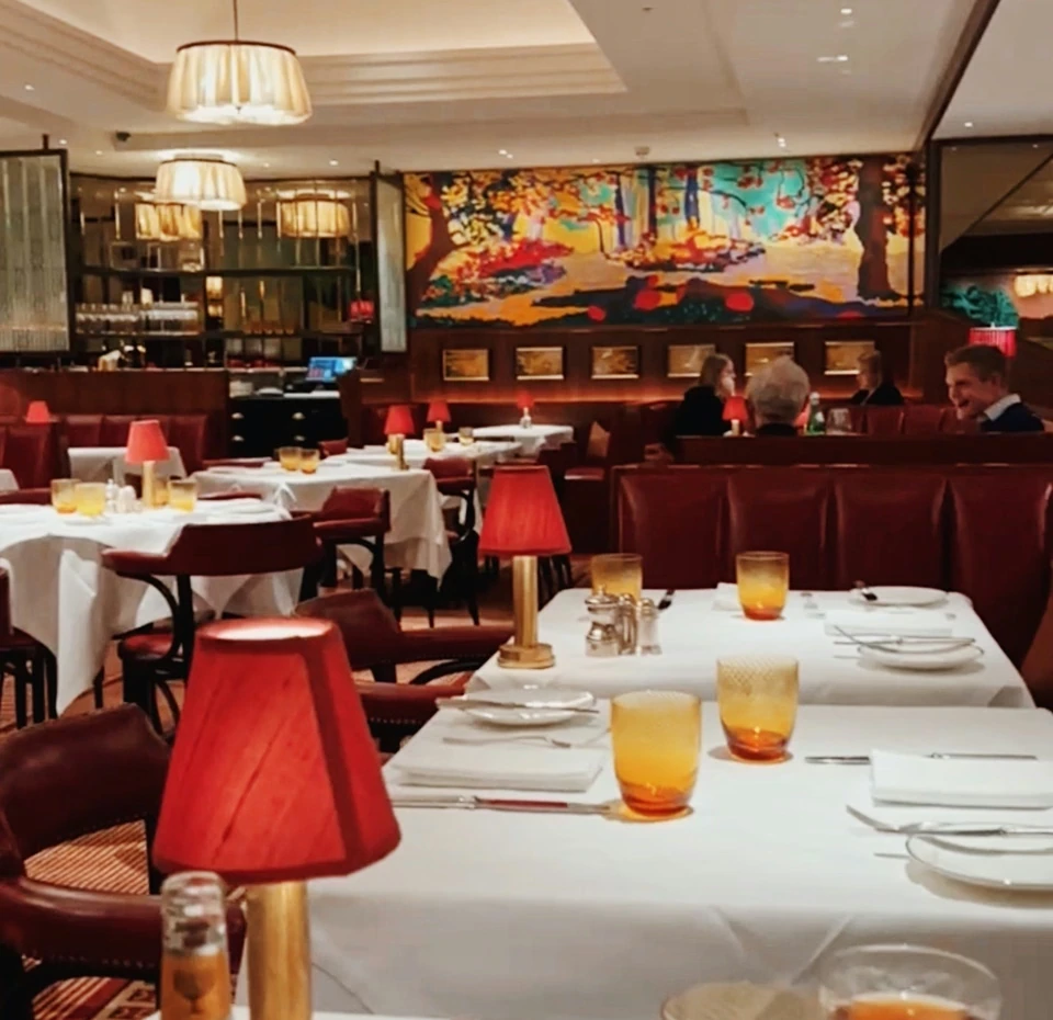 The Colony Grill Room dining room with white tablecloths, red lamps and colourful artwork