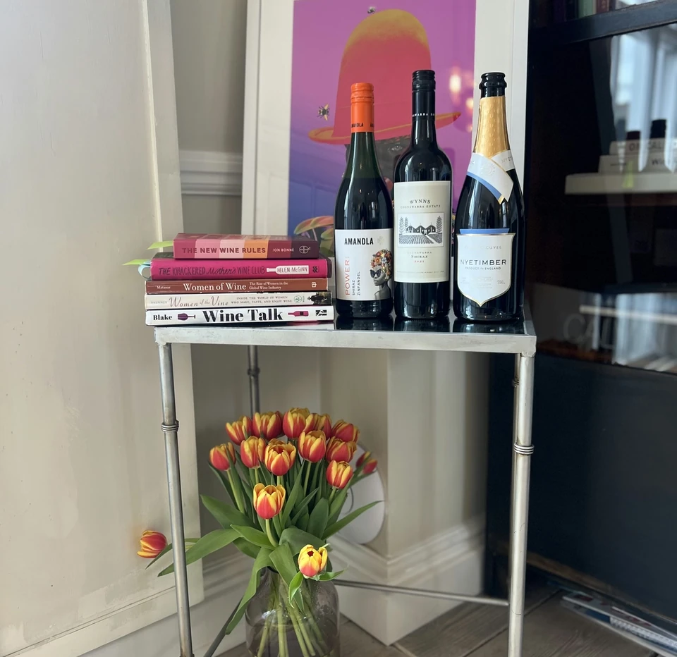 A Nyetimber bottle displayed with two other wine bottles, books about women and wine, flowers and artwork