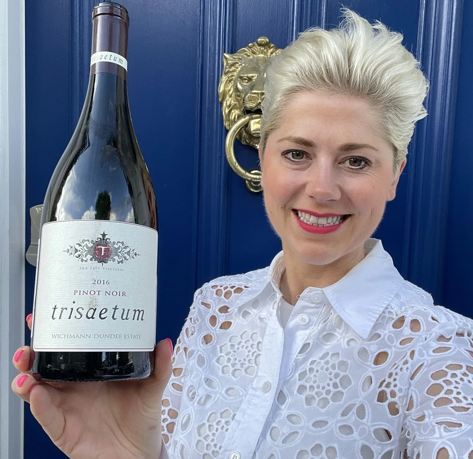 Bottle of Trisaetum 2016 Pinot Noir held in front of a blue door