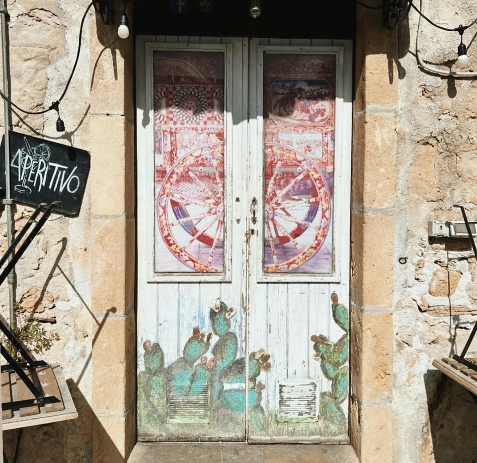 Weathered painted doors beneath string lights, with a chalkboard sign reading Aperitivo