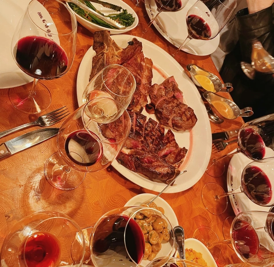 Argentine-style steak dinner surrounded by red wine glasses and side dishes