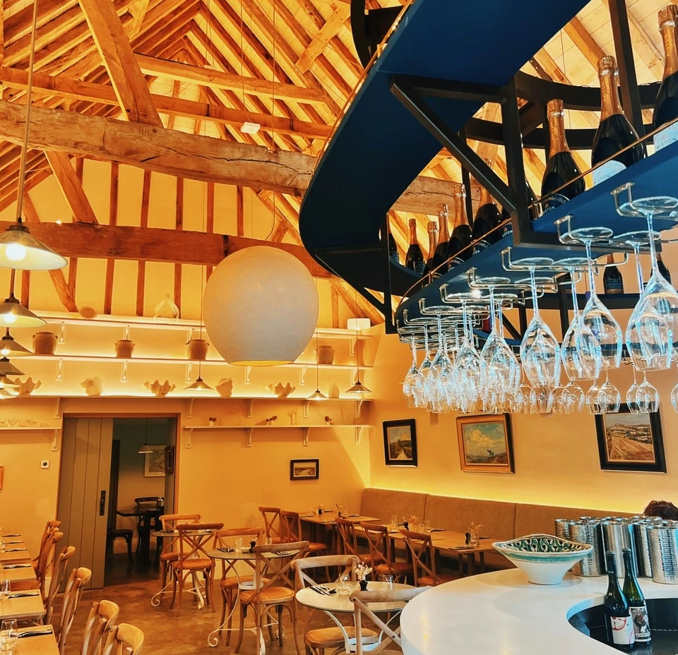 Warmly lit Wiston restaurant interior with timber beams, a curved bar and hanging wine glasses