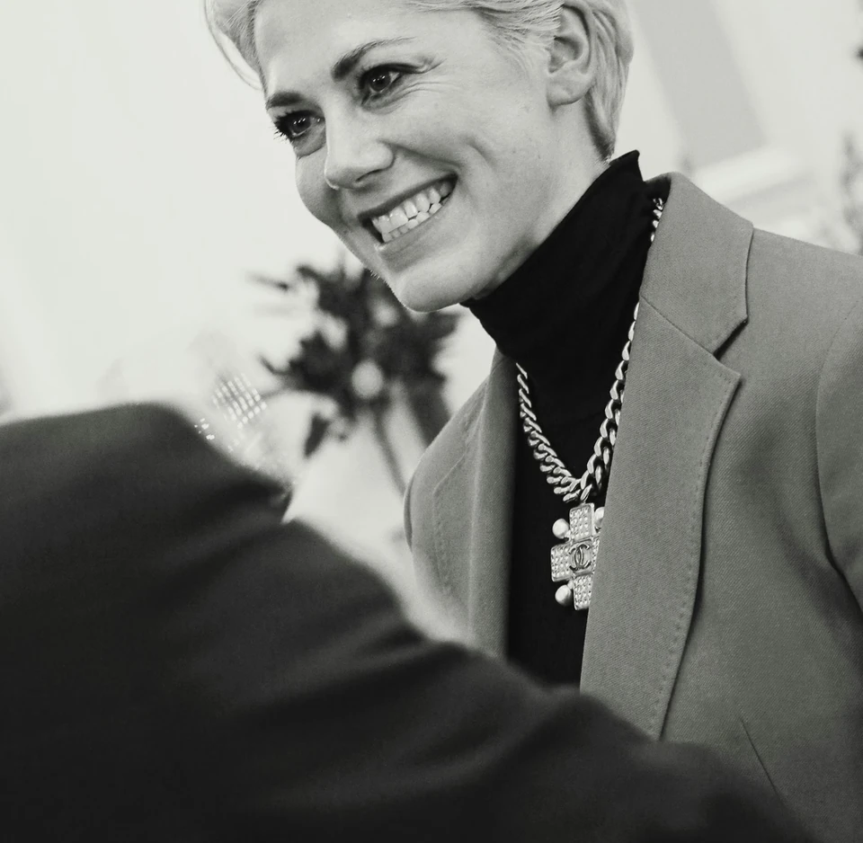 Smiling woman in a blazer and statement necklace at an indoor Champagne event