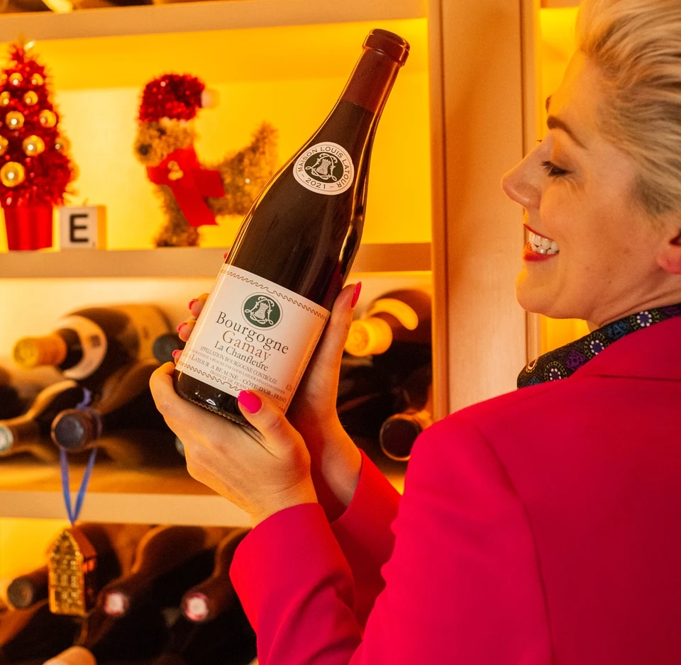 Elizabeth holding a bottle of Bourgogne Gamay in front of a wine rack