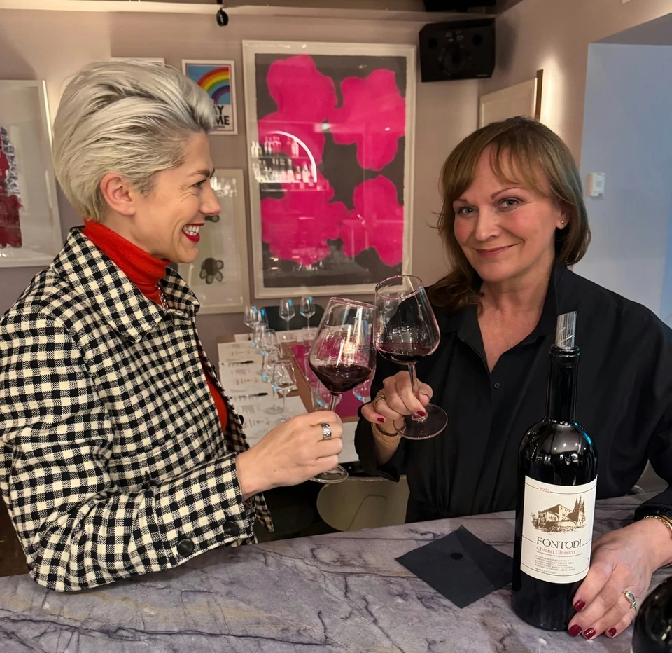 Two women raising glasses of red wine beside a bottle of Fontodi Chianti Classico