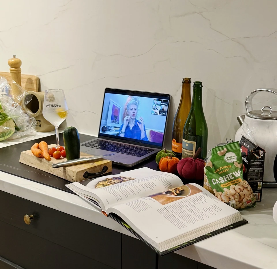 Home tasting setup with wine bottles, glasses, food and a laptop showing a virtual wine presentation.