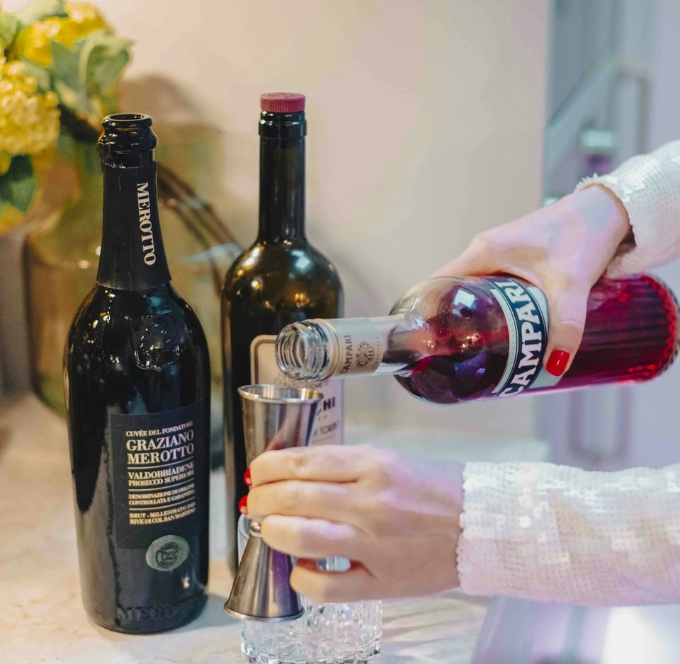 Campari is poured beside bottles of Merotto Prosecco