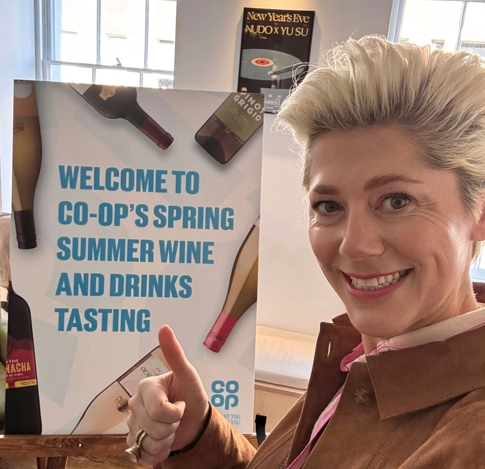 Woman gives a thumbs-up beside a Co-op spring and summer wine and drinks tasting sign