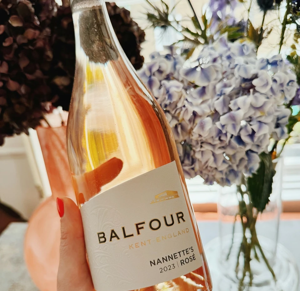 Hand holding a bottle of Balfour Nannette's Rosé 2023 in front of blue and white flowers
